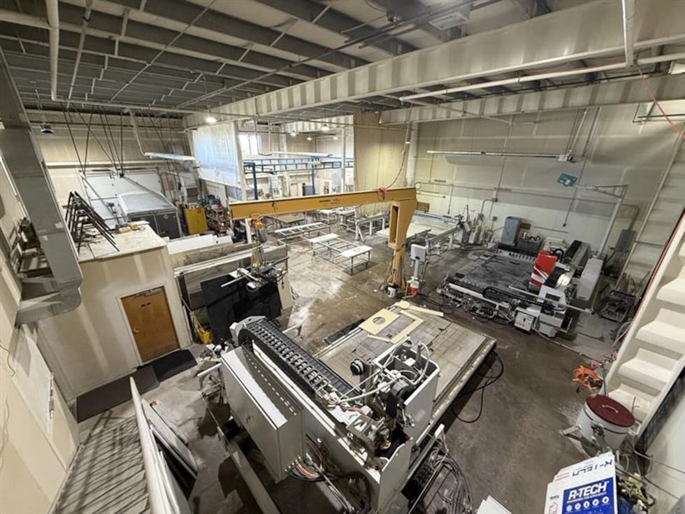 Stone cutting equipment sits in a fabrication facility where workers process engineered stone...